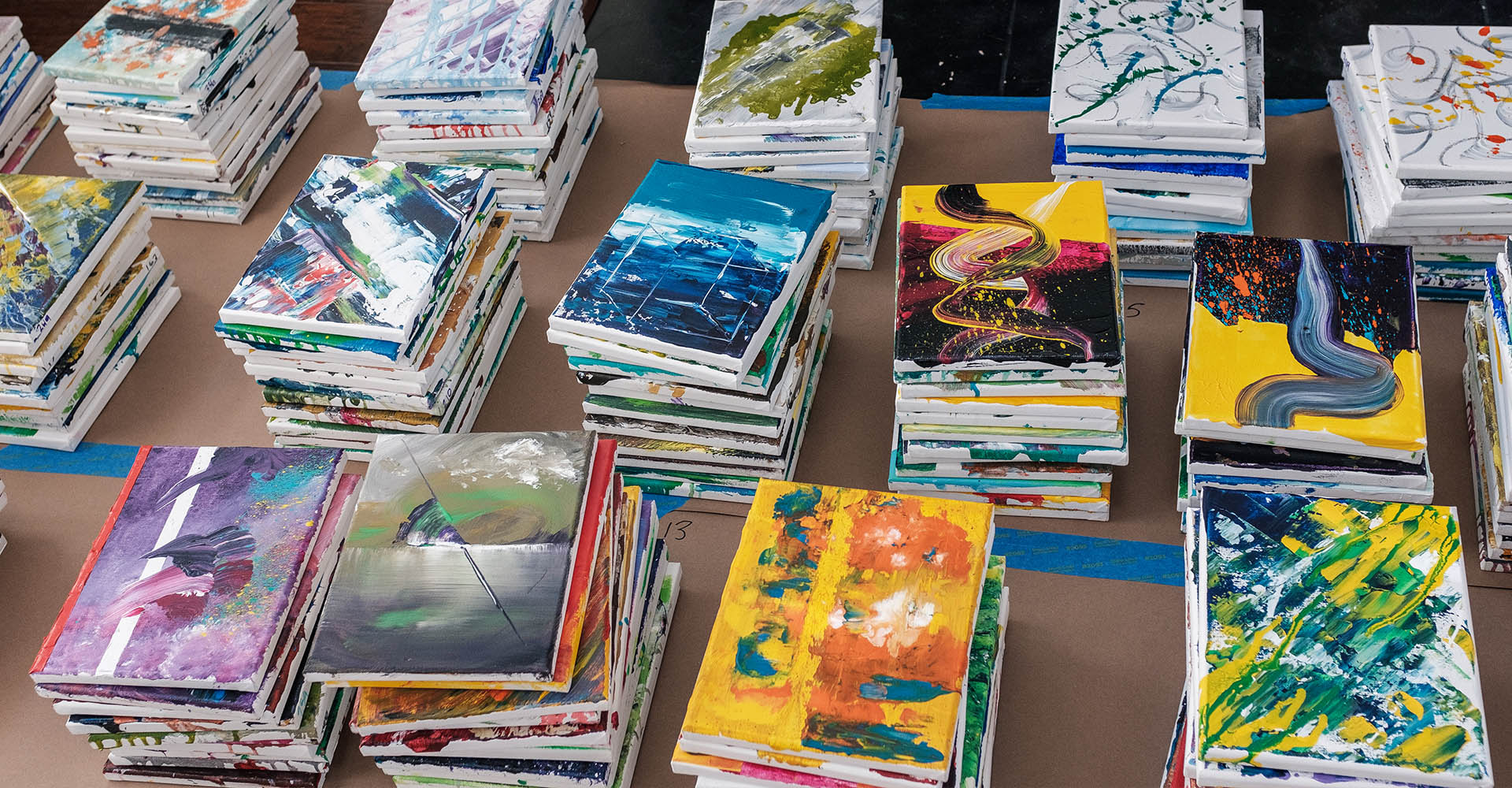 Stacks of paintings spread across a table — the physical reality of 365 days